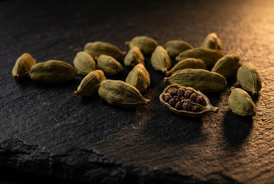 Cardamom pods on dark stone, one cracked open